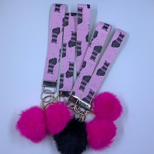 May include: Five pink keychains with black and white illustrations of fists and the text "Black Lives Matter". Each keychain has a fluffy pink pom-pom attached.