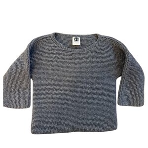 May include: A gray knit sweater with a crew neck and three-quarter length sleeves. The sweater has a textured appearance and a small tag at the back of the neck.