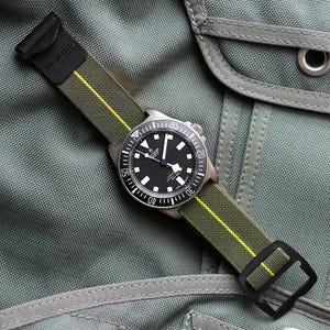 May include: A black-faced wristwatch with a stainless steel case and a green and yellow striped nylon strap. The watch has white hour markers and hands, and a black rotating bezel. The strap is secured with a black buckle.