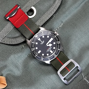 May include: A black and silver watch with a green and red nylon strap. The watch face has a black background with white markings and the word "TUDOR" in white.
