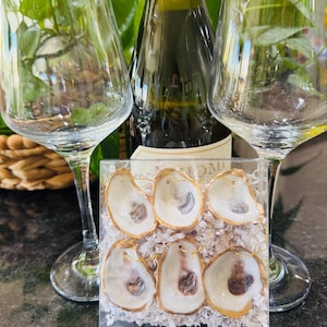 May include: Six gold-rimmed oyster shell ornaments in a clear plastic box with white tissue paper. The ornaments are white with a brown interior and have a gold wire loop for hanging.