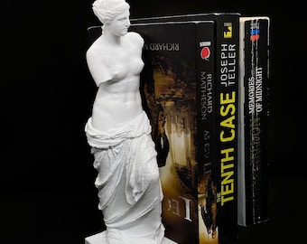 Könnte beinhalten: Weiße Plastikstatue der Venus von Milo, die als Buchstütze verwendet wird und zwei Bücher hält. Das Buch links trägt den Titel "The Tenth Case" von Joseph Teller. Das Buch rechts trägt den Titel "Memories of Midnight" von Richard Matheson.