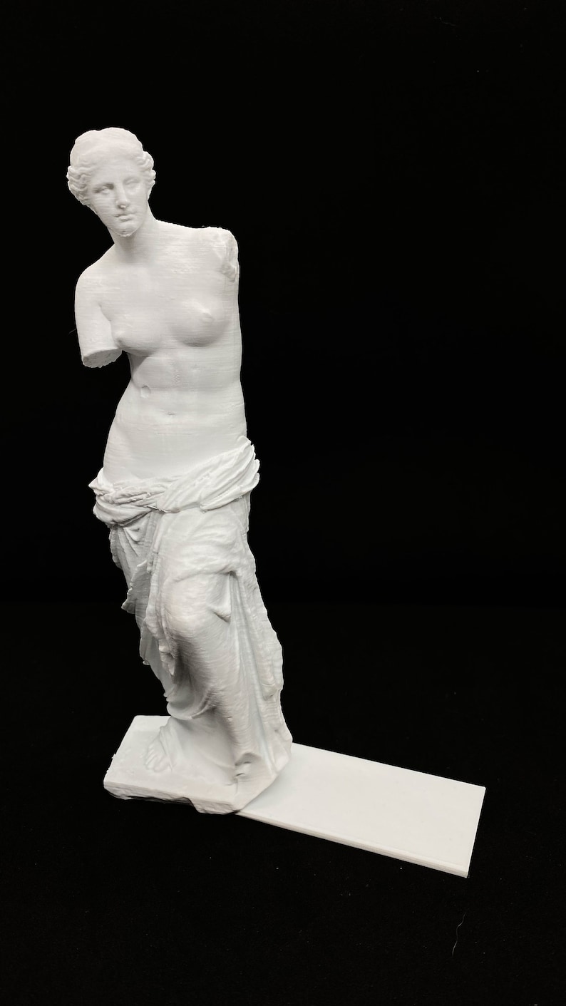 May include: White 3D printed statue of the Venus de Milo, a famous Greek sculpture. The statue is standing on a white base.
