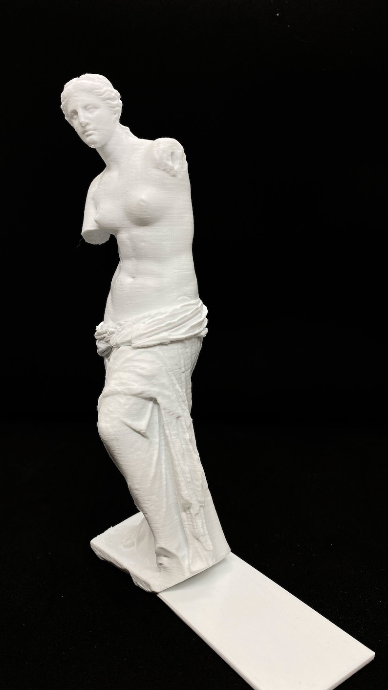 May include: A white 3D printed statue of the Venus de Milo, a famous Greek sculpture. The statue is missing its arms and is standing on a white base.