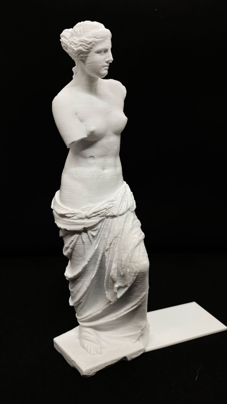 May include: White 3D printed statue of a woman standing on a white base. The statue is a replica of the Venus de Milo, a famous Greek sculpture.