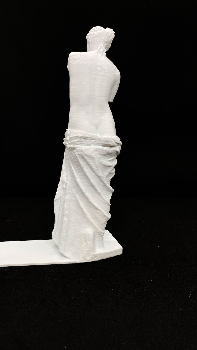 May include: White 3D printed statue of a woman standing with her arms crossed and a draped cloth around her waist.