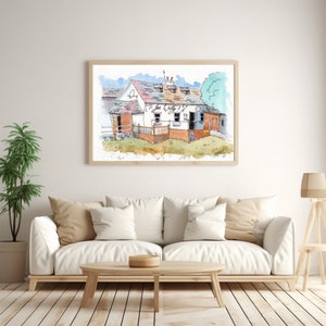 May include: Watercolour painting of a building with the text "Ti Joe Watty's!". The artwork is framed in a light wood frame and hangs above a white sofa with beige cushions. A potted plant and a wooden side table with a lamp are also in the room.