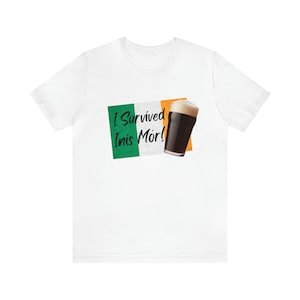 May include: White t-shirt with the text "I Survived Inis Mór!" in green and white, alongside an Irish flag and a pint of dark beer. A casual wear item.