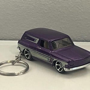 May include: A purple die-cast station wagon toy car keychain featuring silver side panels, black wheels with silver rims, and a circular metal split ring attached to the rear bumper. The vehicle has a metallic finish and a clear windshield.