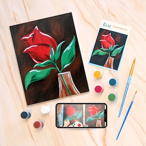 May include: A paint-by-numbers kit featuring a single red rose in a vase. The kit includes a canvas, paints, and brushes. The image also shows a phone displaying a video tutorial.