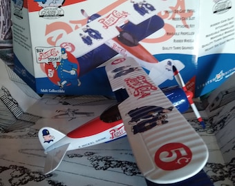 May include: A white and blue die-cast model airplane with a red stripe and "Pepsi-Cola" printed on the side. The airplane has a propeller and wheels. The box says "Limited Edition" and "Modified Stearman 1932".