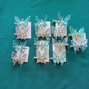 May include: A set of 12 butterfly hair clips in various colors, including blue, pink, green, and silver. The clips are made of metal and have a butterfly design with glitter accents.