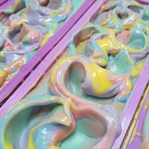 Op de afbeelding: Een close-up van een kleurrijke werveling van zeep in een paarse vorm. De zeep is een mix van roze, paars, geel en blauw.