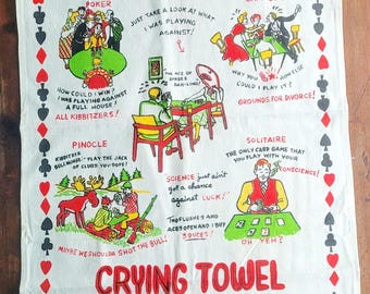 May include: White cotton crying towel with red and black playing card suit borders. The towel features humorous illustrations of card games like poker and canasta, with text like "I got blitzed!" and "My wife is a poker widow!"