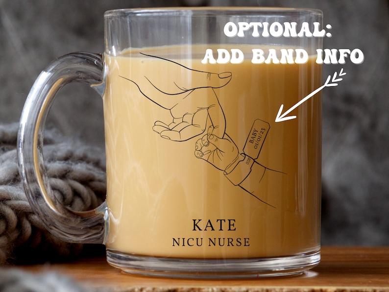 May include: A clear glass mug with a handle, filled with a light brown liquid. The mug has a black line drawing of two hands holding each other, with the text "KATE NICU NURSE" below. A small tag with the text "BABY 01/01/23" is on the wrist of the smaller hand.