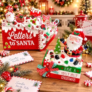 May include: A red metal mailbox with white text reading Letters to SANTA, topped with faux white frosting and holiday ornaments. Beside it, a stack of books with a Santa figure, green tree, and text reading HAVE A HOLLY JOLLY CHRISTMAS.