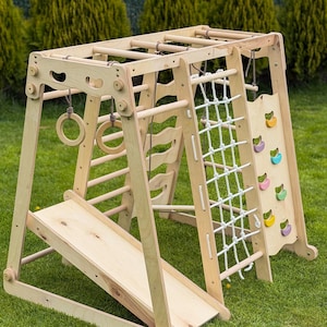 Könnte beinhalten: Ein hölzernes Klettergerüst für Kinder mit Rutsche, Kletternetz, Leiter und Ringen. Der Rahmen ist aus hellem Holz gefertigt und enthält farbige Klettergriffe. Auf grünem Gras.