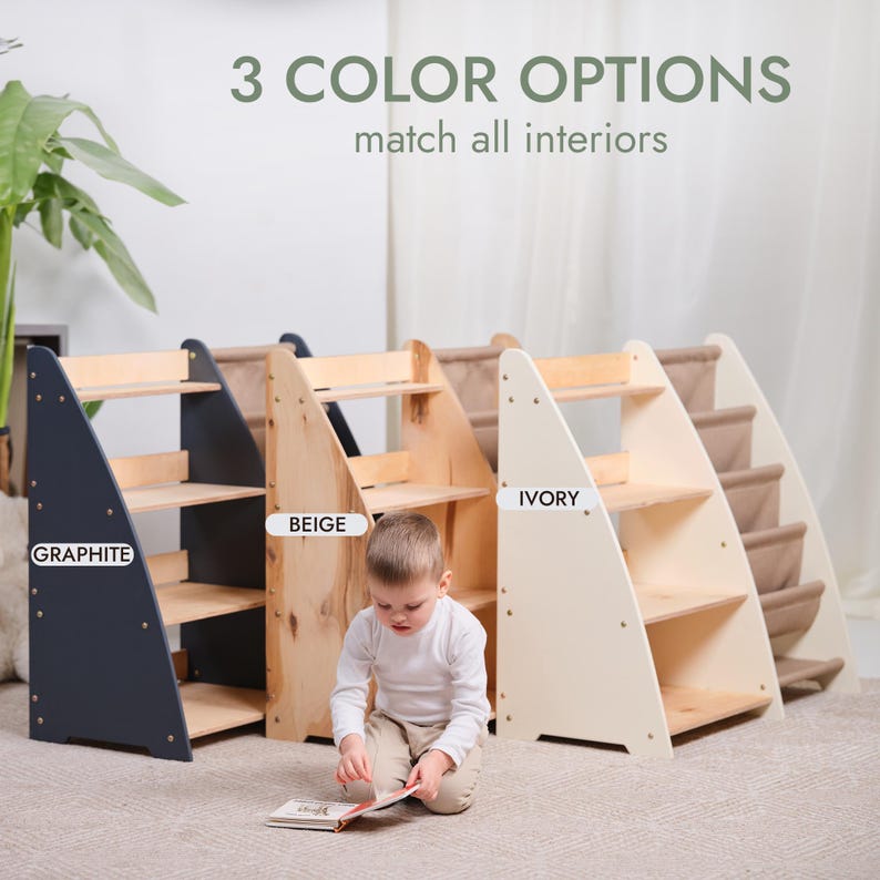 May include: Three wooden climbing structures in graphite, beige, and ivory. Each has a triangular frame with shelves and a ramp. The text reads "3 COLOR OPTIONS match all interiors". A child is sitting in front of the structures.