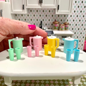 May include: Miniature kitchen set featuring a mint green, pink, yellow, and blue pitcher with matching glasses. The set is displayed on a white table, with a kitchen backdrop.