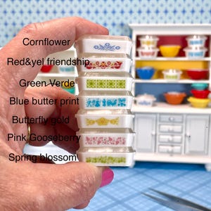 May include: A stack of miniature Pyrex-style dishes in various patterns and colors, including blue, red, green, and yellow. The dishes are held in a hand, with a miniature cabinet in the background. The text on the image lists the names of the patterns.