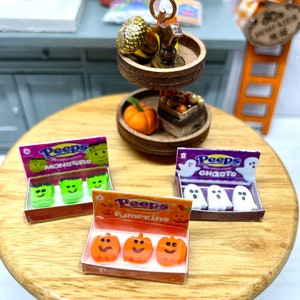 May include: Three boxes of miniature Peeps marshmallow candies. The boxes are labeled "Monsters", "Ghosts", and "Pumpkins". Each box contains three candies with Halloween-themed designs.