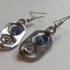 May include: A pair of earrings made from recycled aluminium pull tabs. Each earring features a blue stone and a silver charm with a sun design. The earrings are attached to silver hooks.