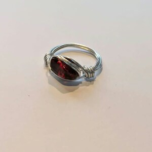 May include: A silver wire wrapped ring with a dark red gemstone.