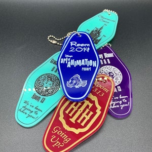 May include: A collection of five colorful hotel keychains with different designs. The keychains feature the text "Room 2014", "Disney's Art of Animation Resort", "Room 13", "Room 1313", and "Going Up?" The keychains are made of plastic and have a shiny finish.