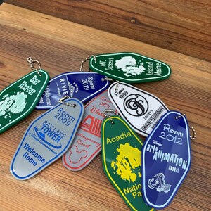 May include: A collection of colorful keychains shaped like hotel room keys. Each keychain features a different Disney resort, including Bay Lake Tower, the Contemporary Resort, Disney's Grand Floridian Resort & Spa, and Disney's Art of Animation Resort. The keychains are made of metal and have a shiny finish.