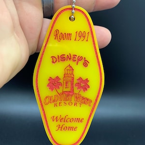 May include: Yellow key chain shaped like a hotel room key with red text that reads "Room 1991", "Disney's Old Key West Resort", and "Welcome Home".