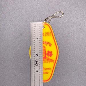 May include: Yellow plastic key chain with a red and white lighthouse design. The keychain says "Disney's Port West Resort" and "Welcome Home" in red text. The keychain also says "Fall 1991".