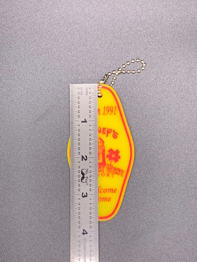 May include: Yellow plastic key chain with a red and white lighthouse design. The keychain says "Disney's Port West Resort" and "Welcome Home" in red text. The keychain also says "Fall 1991".
