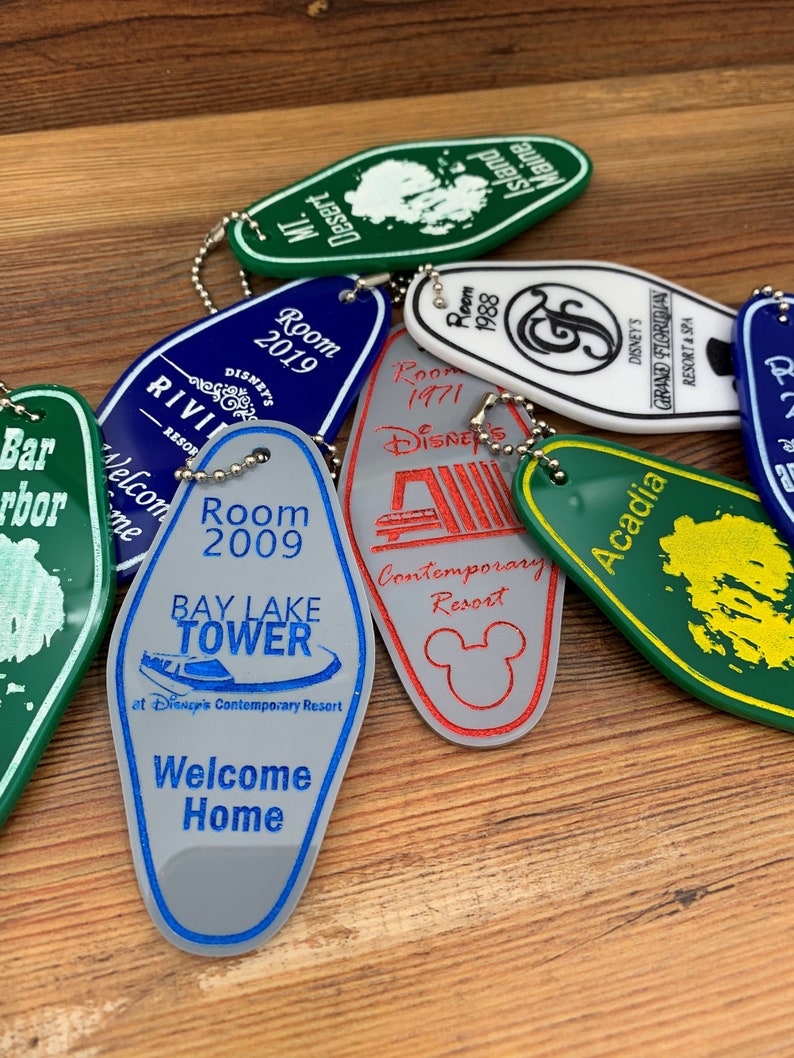 May include: A collection of colorful Disney resort hotel keychains. The keychains are shaped like hotel room keys and feature the names of the resorts, including Bay Lake Tower, Contemporary Resort, Grand Floridian Resort & Spa, and Acadia. The keychains are made of plastic and have a silver metal ring.