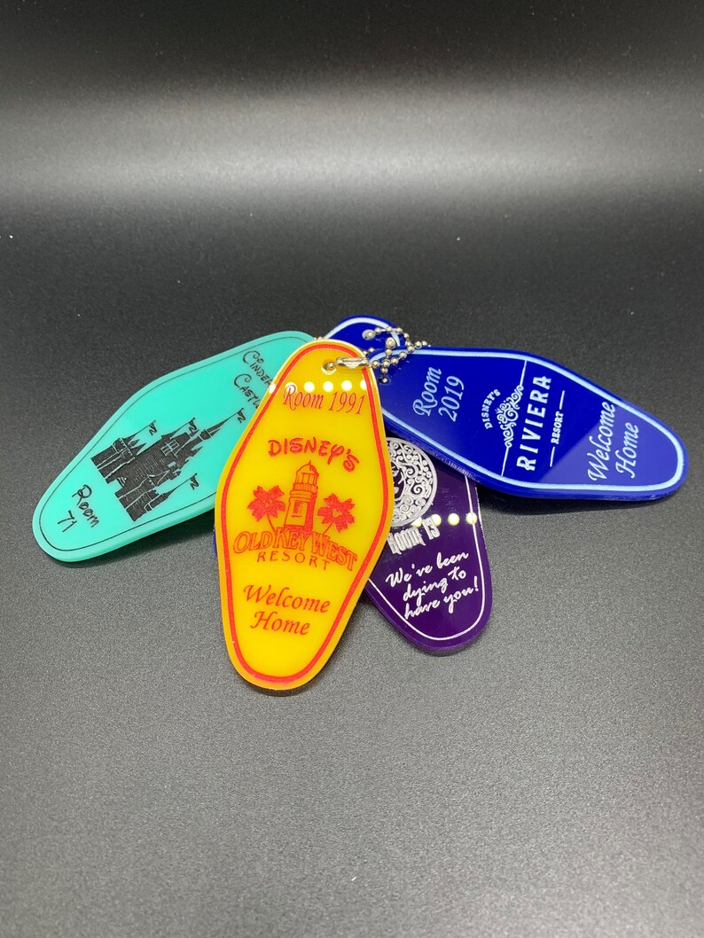 May include: A collection of four colorful hotel keychains with the words "Disney's Old Key West Resort", "Welcome Home", "Room 2019", and "Riviera Resort" printed on them.