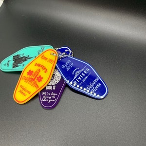 May include: Four colorful keychains with different designs. The keychains are shaped like hotel room keys and feature the words "Disney's", "Old West Resort", "Riviera Resort", and "Welcome Home".