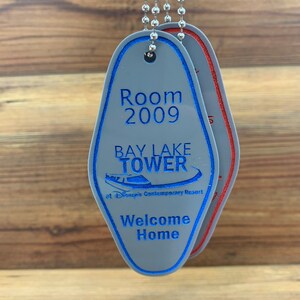 May include: A gray key chain with a blue and white hotel key tag. The key tag has the text "Room 2009", "Bay Lake Tower", "at Disney's Contemporary Resort", and "Welcome Home".