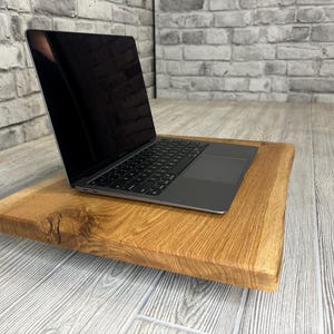 May include: A laptop computer rests on a wooden laptop stand. The stand is crafted from natural wood with a rustic finish. The laptop is closed and has a black screen.