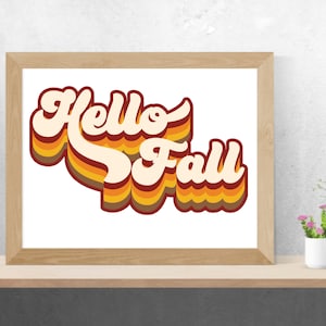 May include: A framed print featuring the text "Hello Fall" in a retro 70s style font with orange, yellow and brown stripes.