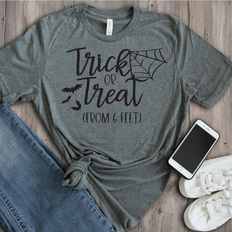May include: A heather grey t-shirt with the text "Trick or Treat (From 6 Feet)" in black. The shirt features a spiderweb and bats.