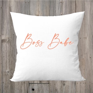 May include: White pillow with the text "Boss Babe" in a coral pink cursive font.