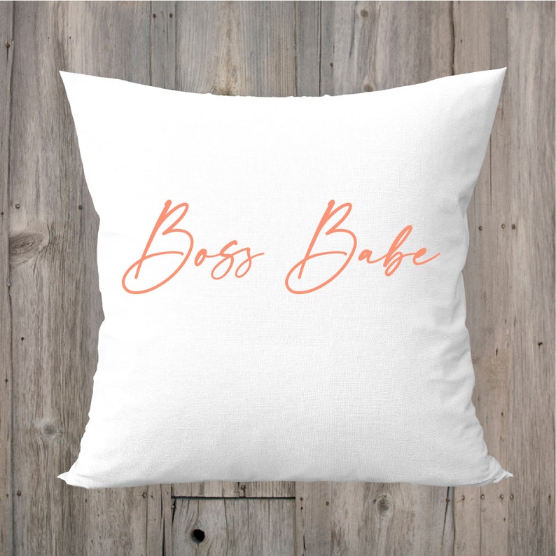 May include: White pillow with the text "Boss Babe" in a coral pink cursive font.