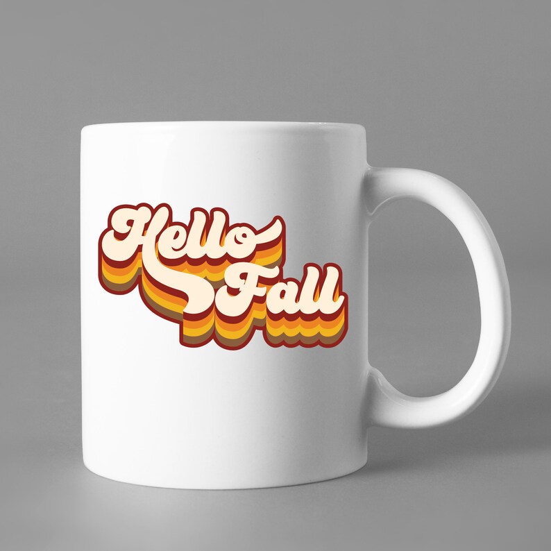 May include: White ceramic mug featuring a retro-style graphic that reads "Hello Fall" in orange, yellow, and red.