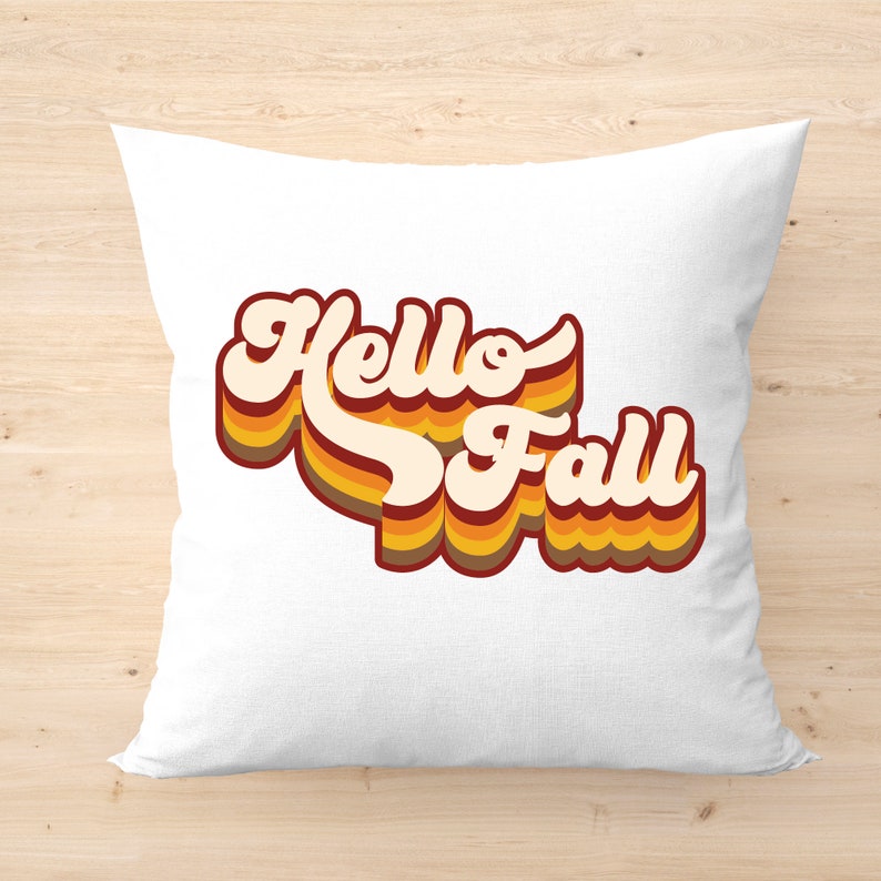 May include: White throw pillow with the text "Hello Fall" in a retro 70s style font with orange, yellow, and brown stripes.