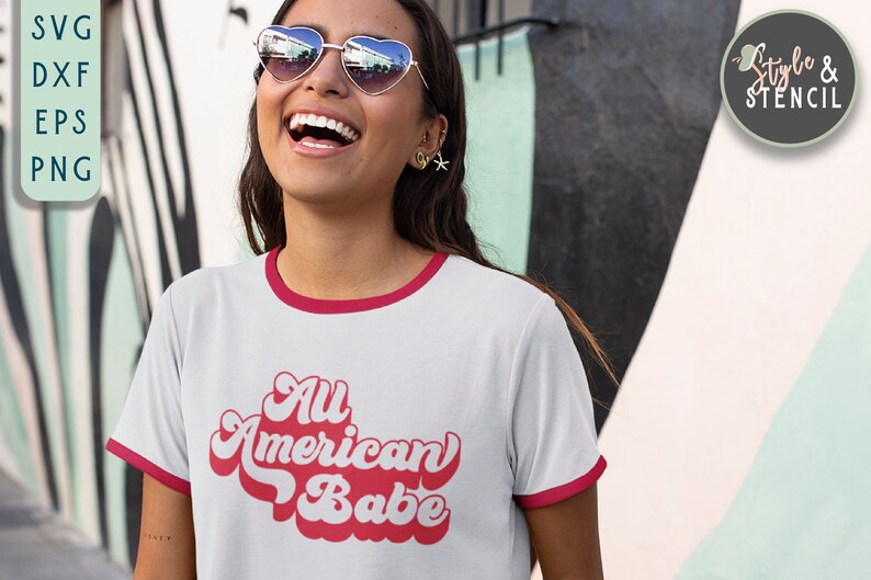 May include: A white t-shirt with a red ringer neckline and a red retro-style graphic that says "All American Babe".