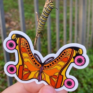 Puede incluir: Una pegatina de un par de patines de ruedas naranja y amarillo con ruedas rosas y un diseño de mariposa. La pegatina está en una rama con una oruga negra y amarilla.