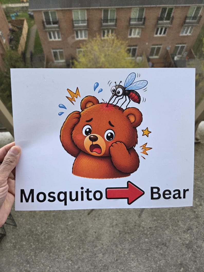 Pode incluir: Uma placa branca com uma ilustra&ccedil;&atilde;o de desenho animado de um urso marrom sendo picado por um mosquito. O urso tem uma express&atilde;o surpresa, com as palavras "Mosquito Bear" e uma seta apontando para o urso.