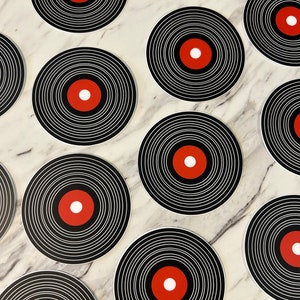 Może przedstawiać: Zbi&oacute;r czarno-białych podkładek pod kubki w kształcie płyt winylowych z czerwonym środkowym k&oacute;łkiem. Podkładki są ułożone w wz&oacute;r na marmurowej powierzchni.