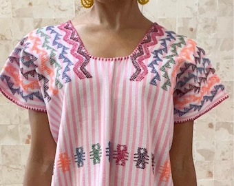 May include: A pink and white striped dress with colorful embroidered details. The dress features short sleeves and a loose fit, with embroidered patterns in various colors. The dress is a casual, comfortable garment.