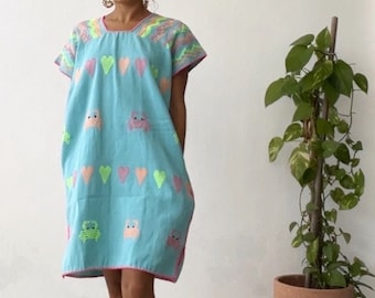 May include: A light blue embroidered dress with pink and green hearts and animal designs. The dress has short sleeves and a scoop neck.