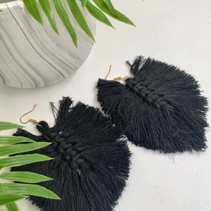 Puede incluir: Un par de pendientes de borla negros con ganchos dorados. Las borlas est&aacute;n hechas de un material suave y tejido y miden aproximadamente 7,5 cm de largo.